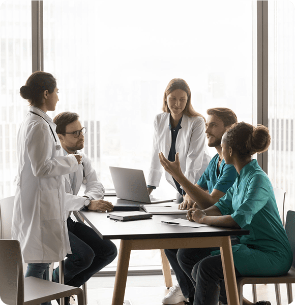 Young clinic chief man talking to diverse staff of doctors at meeting table, giving consultation of expert to listening multiethnic practitioners. Medical colleagues discussing job, treatment case